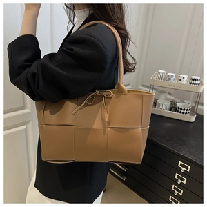 Detail view of large brown woven tote bag featuring a leather bow and tubular handles