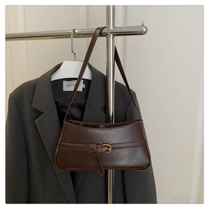 Detail of dark brown leather baguette bag with golden buckle on a clothing rack