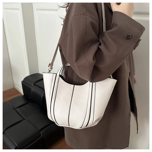 Sac seau blanc avec lignes verticales noires porté sur un manteau brun, style minimaliste