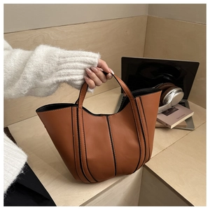 Détail d'un sac seau en cuir marron avec passepoil noir dans un décor de bureau