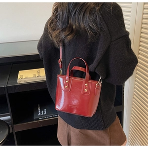 Deep red leather mini bucket bag with gold studs shown in a stylish lifestyle setting