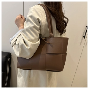 Detail of deep brown woven tote bag featuring large grid pattern and slim shoulder straps