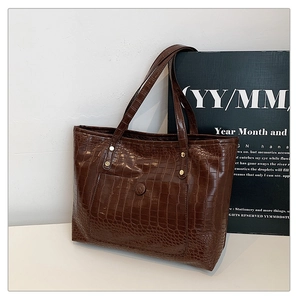 Detailed view of dark brown tote bag featuring premium crocodile embossed texture and rivets