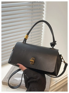 Close-up of black textured leather handbag with a gold twist lock and knot handle