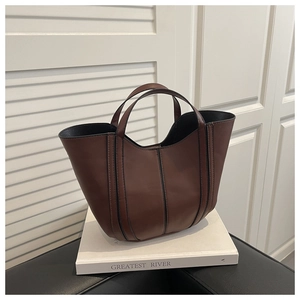 Détail d'un sac seau en cuir marron avec passepoils noirs et poignées robustes à la main