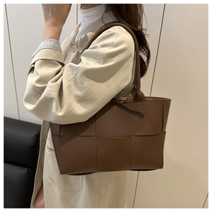 Detail of dark brown woven leather tote bag with wide strap design worn with a trench coat