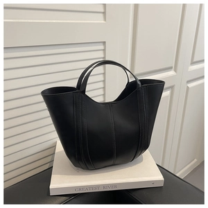 Détail d'un sac seau en cuir noir mat posé sur un livre dans un décor minimaliste moderne