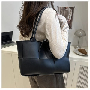 Side view of large black woven leather tote bag with thin shoulder straps on model