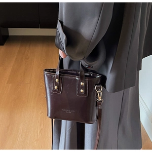 Detail of dark brown polished leather mini bucket bag with gold rivets and handle