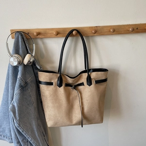 Minimalist large camel suede tote bag with black handles hanging on a wooden rack