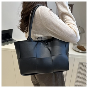 Chic black woven leather tote bag shown on shoulder in a professional office setting