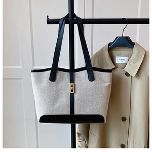Détail du sac cabas en toile avec garniture en cuir noir suspendu à côté d'un trench-coat chic