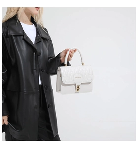 Detail of white quilted handbag with gold metal lock held by a model in black leather