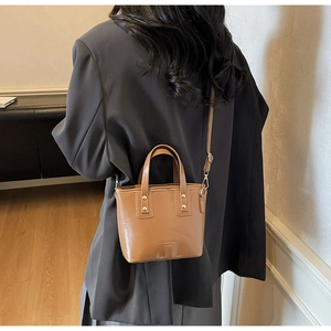 Brown mini bucket bag with gold studs and adjustable strap shown on a model