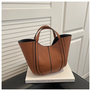 Détail d'un sac seau en cuir marron avec bordure noire sur un livre en décor minimaliste