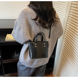 Detail showing the black glossy mini bucket bag with metallic rivets on a grey sweater