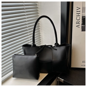 Detailed view of black woven leather tote bag set with matching inner pouch on a windowsill