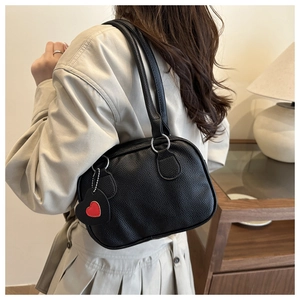 Detail of black litchi texture on handbag with heart-shaped charm and double handles