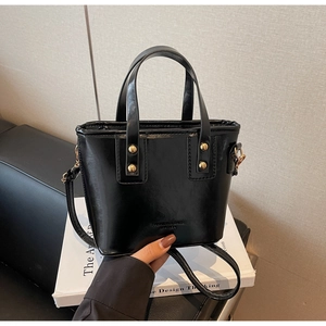 Detail of high-gloss black leather tote bag with gold studs and brand embossing