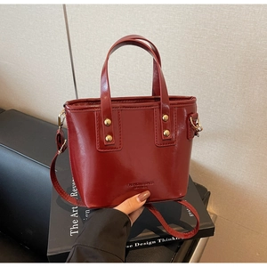 Detail view of burgundy bucket bag with gold rivets on a decorative book background