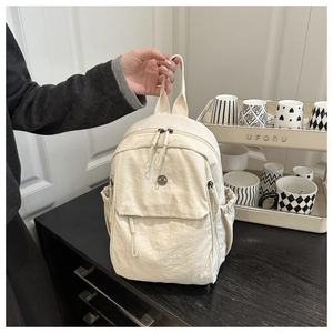 Detail shot of lightweight cream nylon backpack with dual zippers and woven top handle