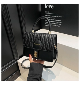 Detail of black leather quilted handbag with gold clasp and fashion logo on the flap