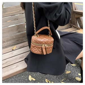 Close-up of caramel brown quilted cylinder bag with gold chain and top handle on a bench