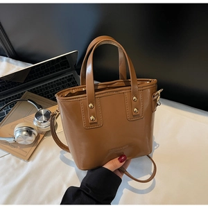 Detailed close-up of brown glossy leather bucket bag with top handles and gold hardware