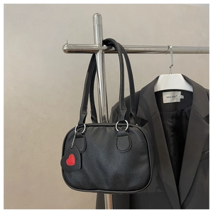 Close-up of black lychee grain leather handbag featuring a red heart charm and chain