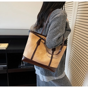 Detail of a large canvas tote bag with brown leather trim shown on a person shoulder