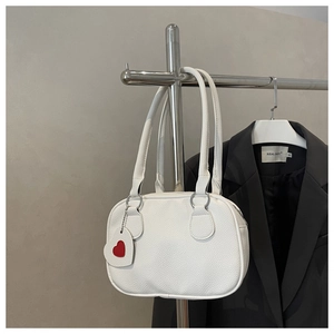 Vertical display of a white pebble leather handbag with a red heart charm on a metal hanger