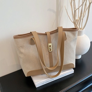 Minimalist beige canvas tote bag with brown leather trim and gold metal lock detail