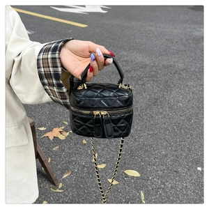 Detail of black quilted leather box bag featuring a top handle and gold chain strap