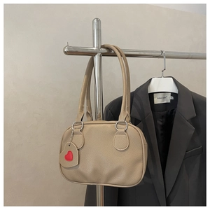 Detail of apricot pebbled leather tote bag featuring a red heart charm and silver metal rings