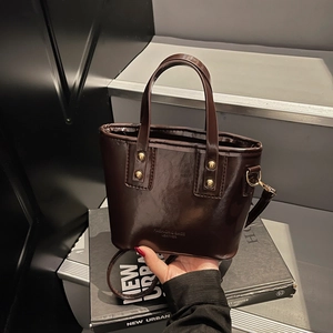 Dark brown glossy mini bucket bag with gold studs and detachable strap in hand