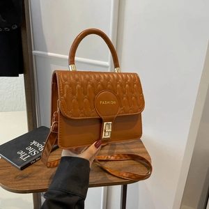 Brown quilted crossbody bag with golden buckle and top handle in a minimalist setting