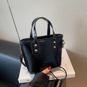 Elegant black glossy leather bucket bag with gold rivets and adjustable crossbody strap