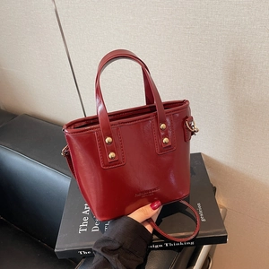 Chic burgundy patent leather bucket bag with gold rivets on a design book background