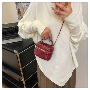 Detail view of burgundy quilted chain bag with gold hardware and top handle on a table
