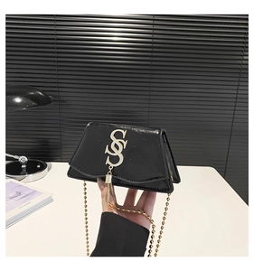 Close-up of black patent leather crossbody bag with gold S-buckle and tassel detail