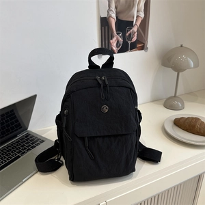 Minimalist black nylon backpack with metal M logo shown on a desk with laptop