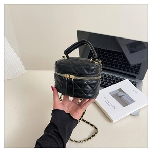 Detailed macro view of black quilted leather stitching and metal chain on compact bag
