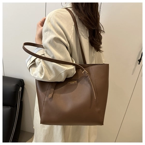 Detail of a large brown leather tote bag with embossed text and adjustable shoulder strap