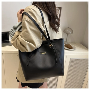 Detailed view of black leather tote bag with gold buckle and embossed logo patch