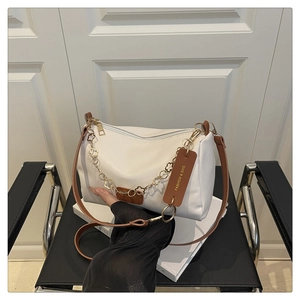 Détail d'un sac bandoulière blanc avec chaîne à fleurs dorées posé sur une chaise