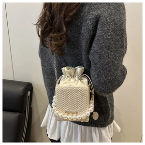 Detail of cream woven bucket bag featuring pearl handle, chain strap, and drawstring closure