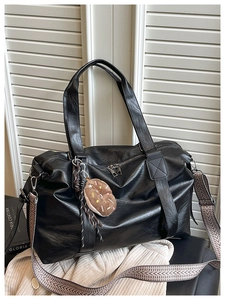 Detail of black soft leather tote bag featuring a textured woven strap and plush charm