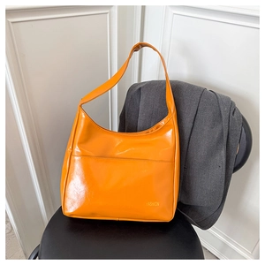 Detail of bright orange hobo bag featuring large front pocket and gold fashion logo