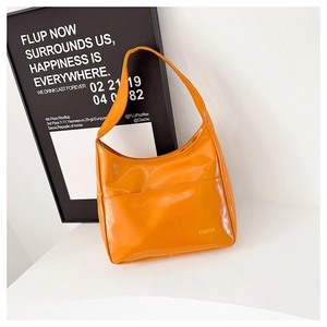 Detail of glossy orange leather tote bag showing front pocket and fashion text print