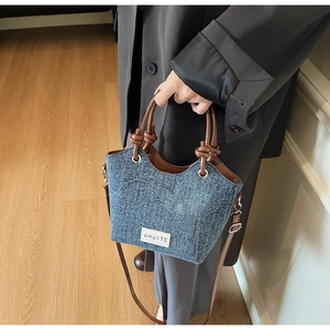 Dettaglio della borsa a secchiello in denim con manico in pelle annodato e patch bianca